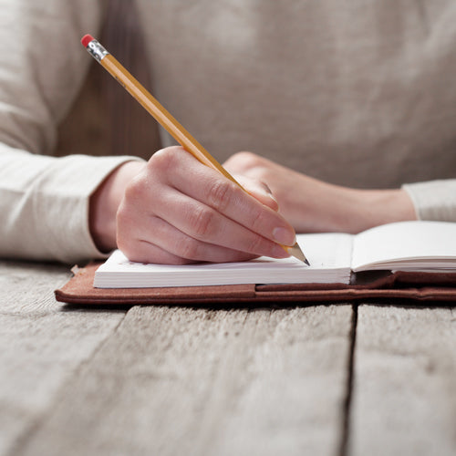 a person is holding a pencil and writing on a notebook